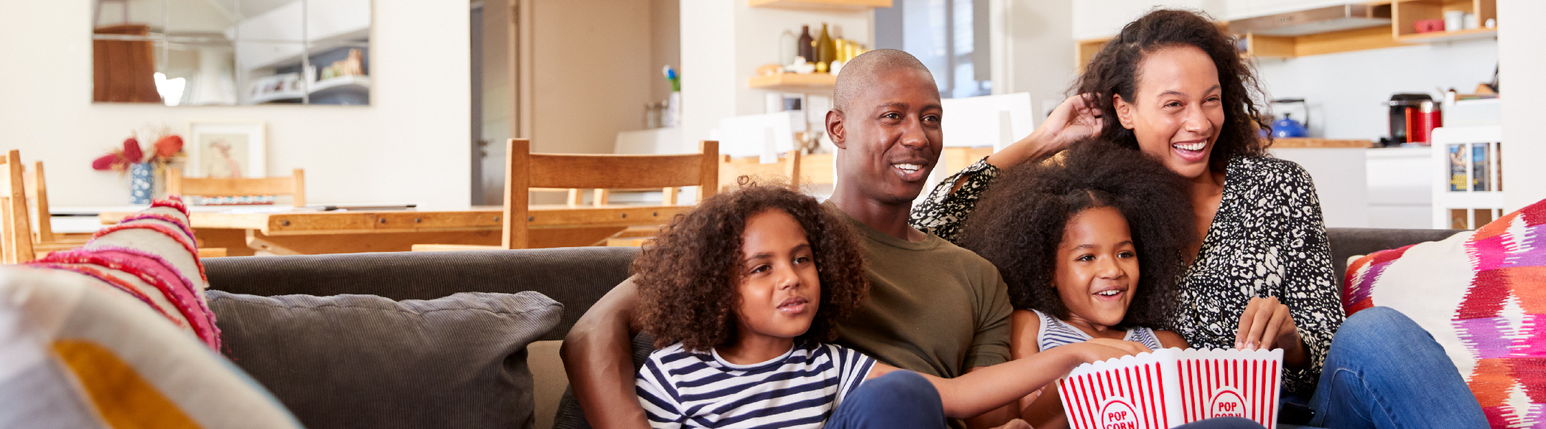 Young family sits closely watching a movie and eating popcorn