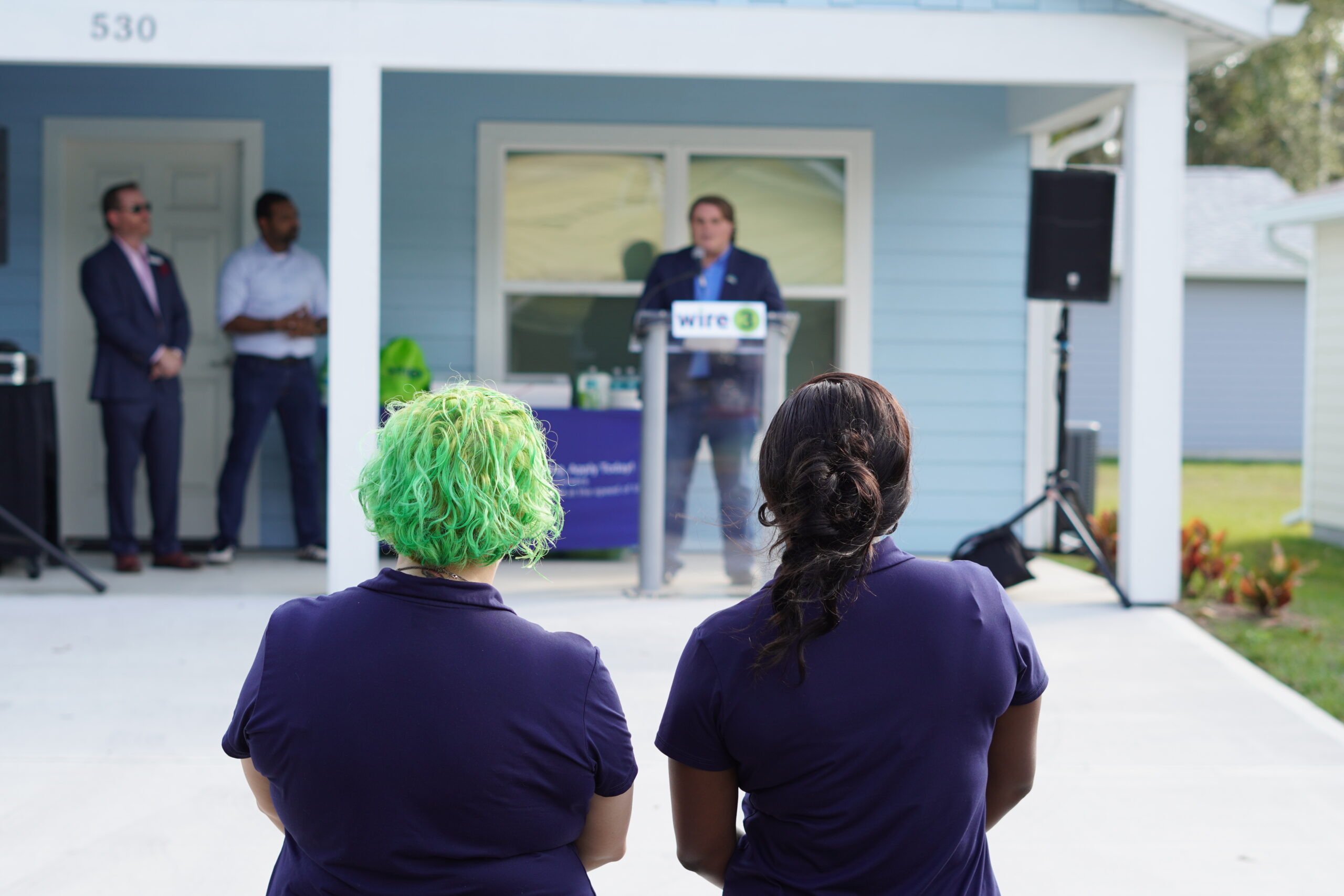 Wire 3 Celebrates a New Home with Habitat for Humanity Attendees listen to a speaker at a podium during a Wire 3 Habitat for Humanity home dedication ceremony