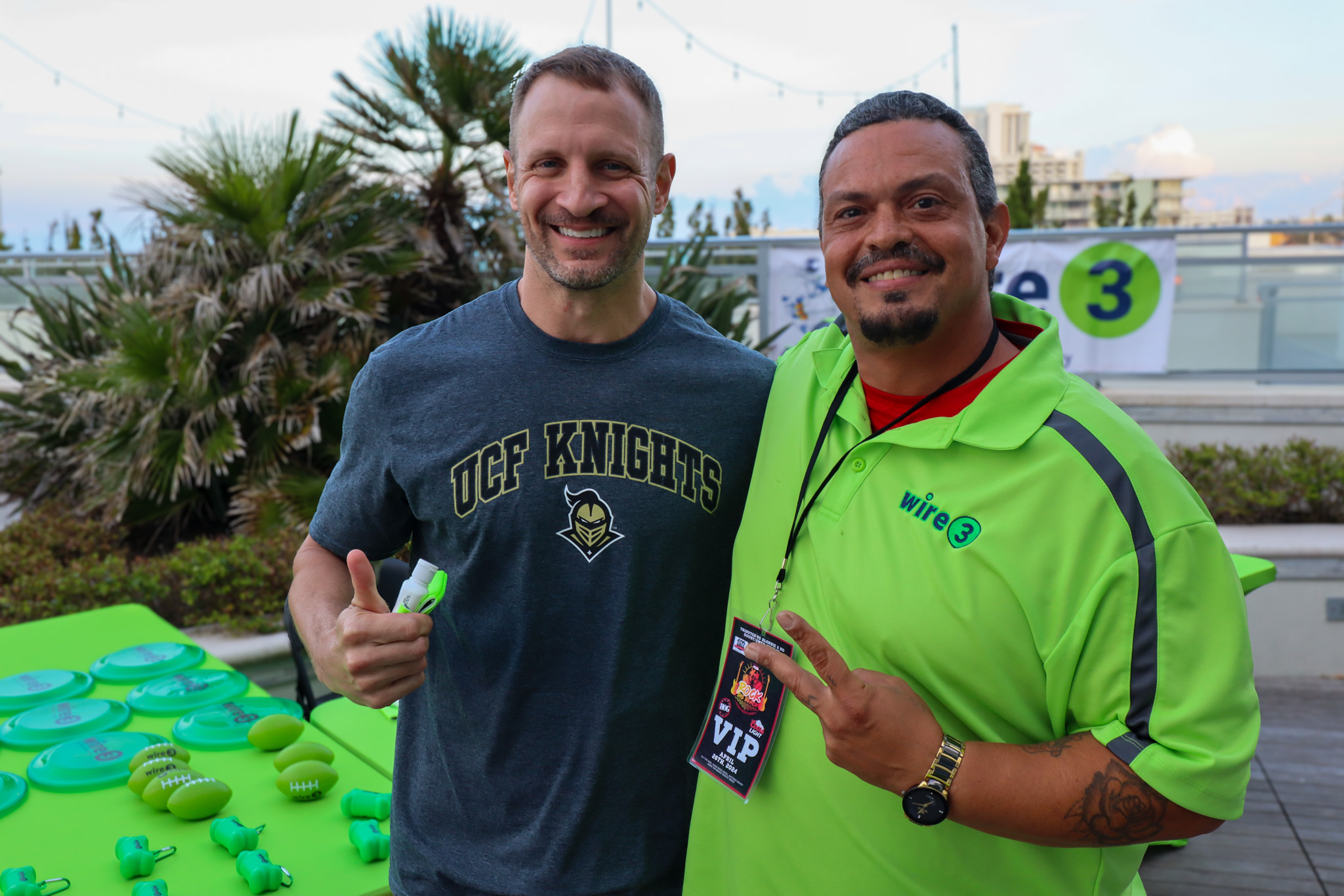 Wire 3 Connects with Fans at a Rooftop Community Event Two men posing together at a rooftop community event, one wearing a UCF Knights shirt and the other in a Wire 3 branded polo