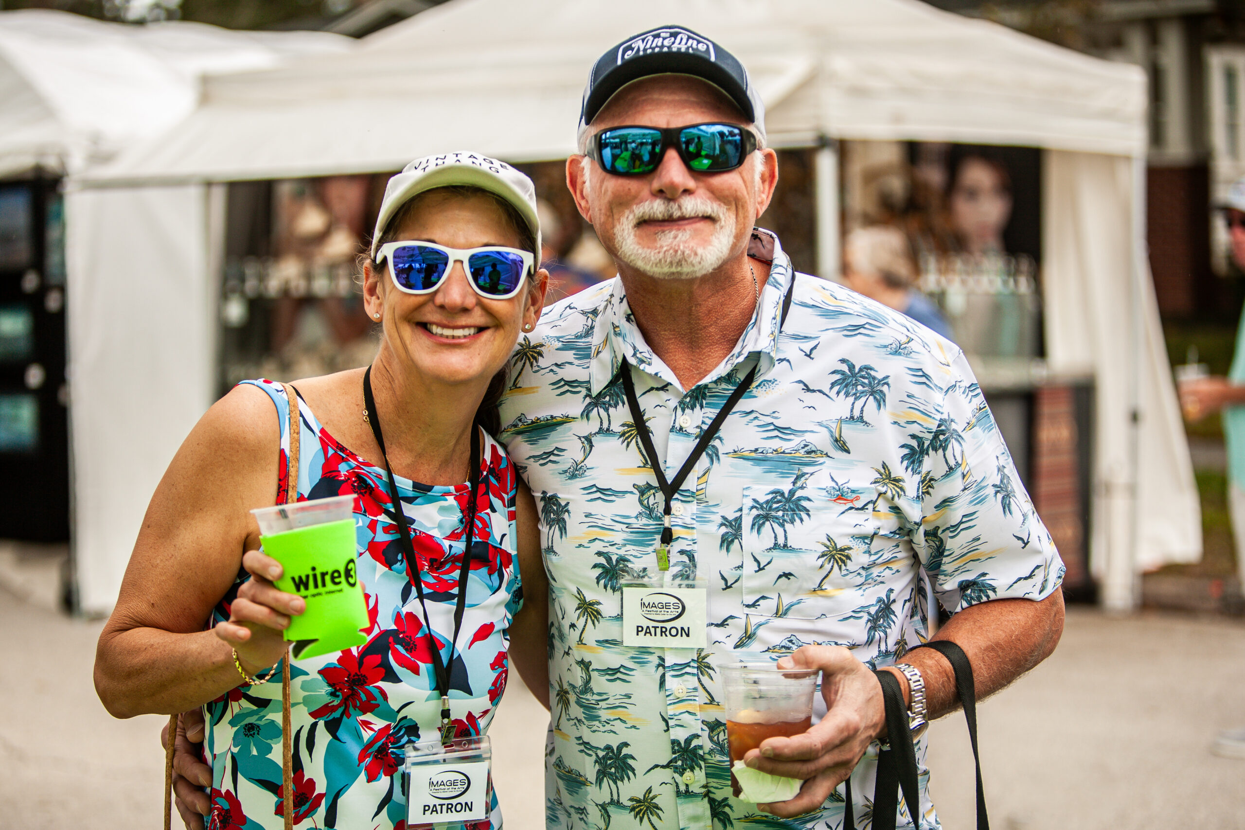 Wire 3 Fans Enjoying a Local Festival Couple in tropical shirts smiling and holding a Wire 3 branded cup at a community festival