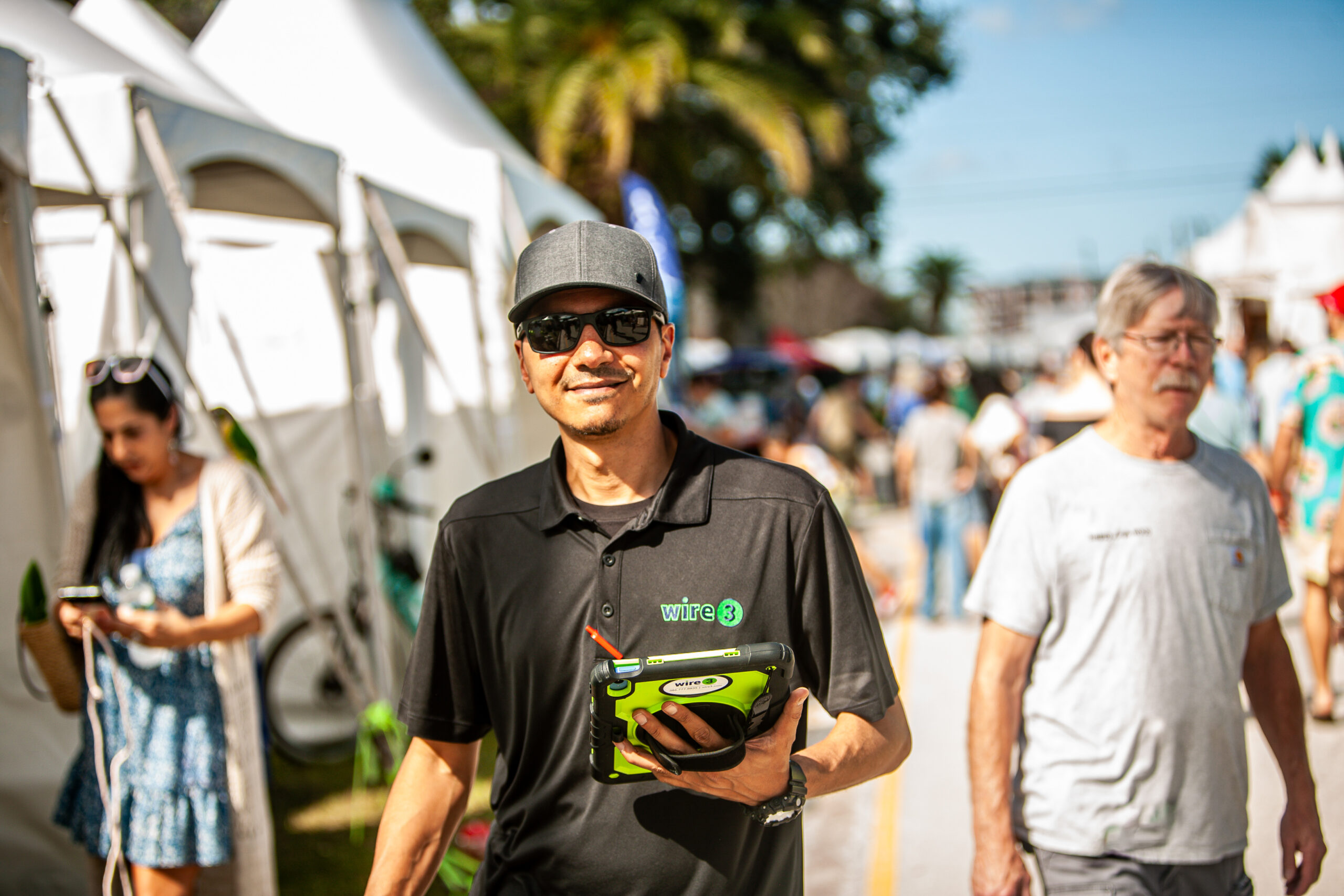 Wire 3 On the Ground at a Local Community Event Wire 3 team member holding a promotional device at an outdoor community event with vendor tents